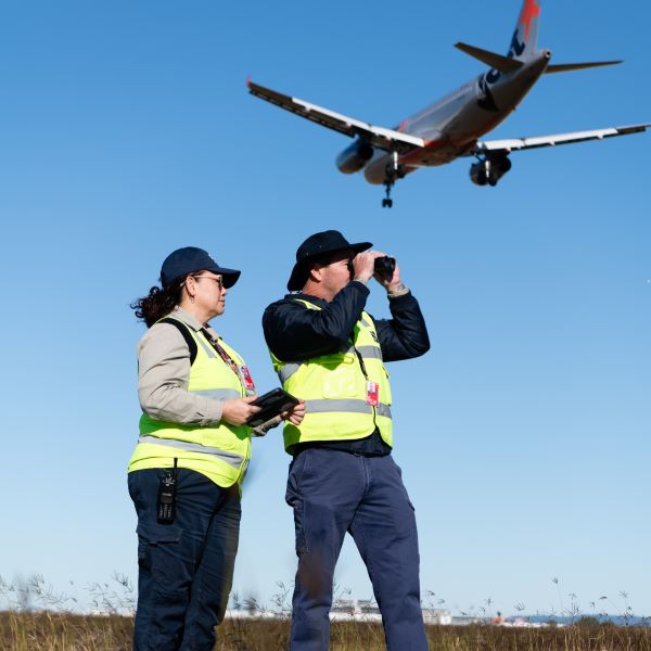 Two airside officers with a Jetstar plane flying overhead