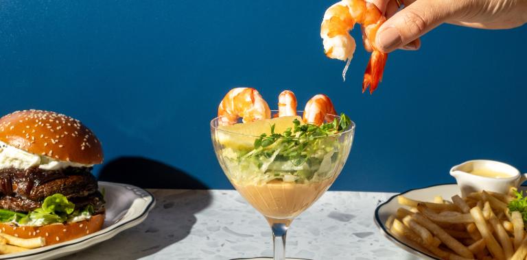 Meals from The Independent presented on small plates with a hand grabbing a prawn