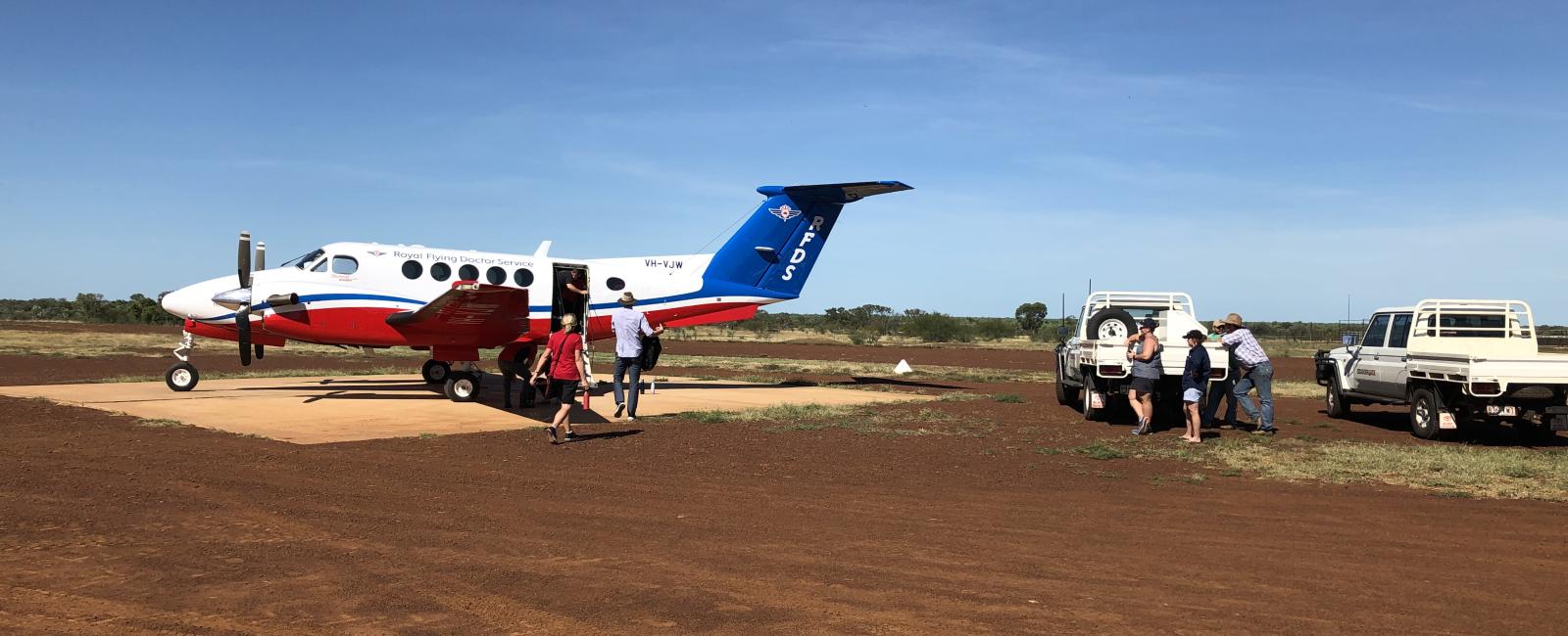 RFDS plane picking up a patient on a red dirt runway with two cars nearby